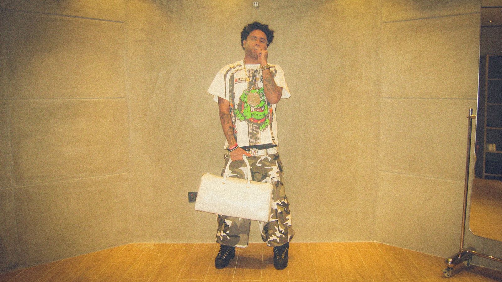 Suono Sai full length in camouflage cargo pants holding a white duffel bag
