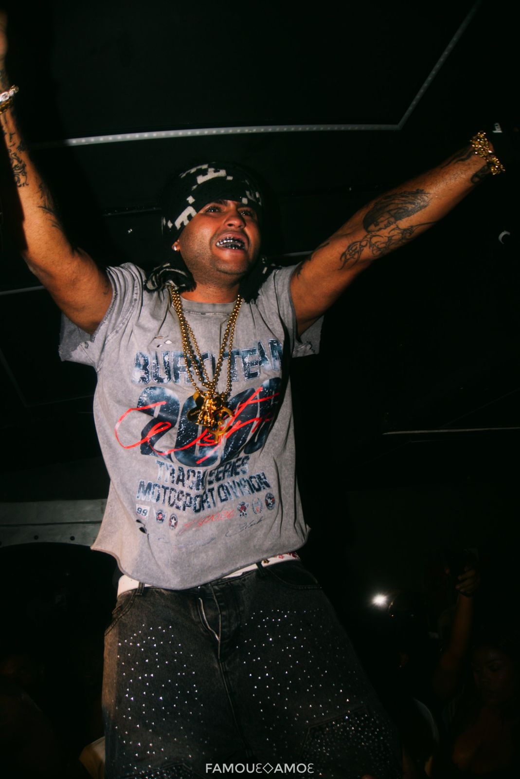 Suono Sai on stage with both arms raised, silver grills and gold chains